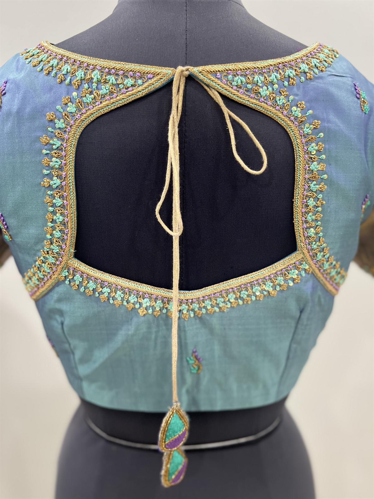 Back of a teal blouse with aari embroidery around a keyhole opening and a tassel tie-back