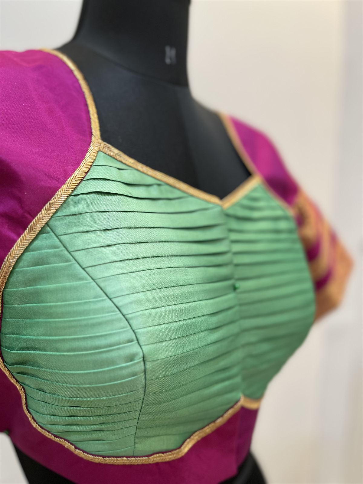 Close-up of a magenta blouse with a sage green pintucked front panel and gold piping